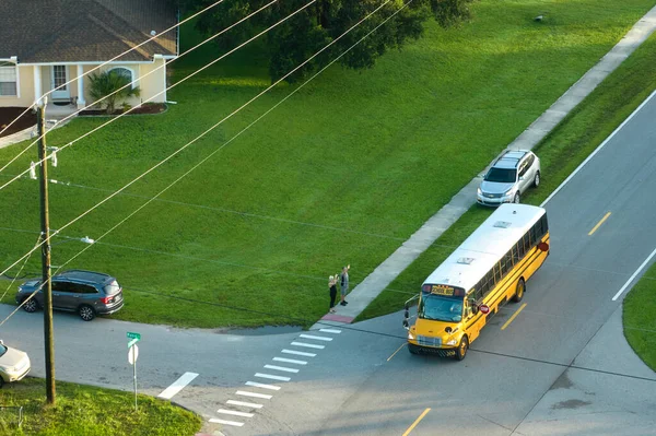 Aerial view of american yellow school bus picking up children at sidewalk bus stop for their lessongs in early morning. Public transportation in the USA.