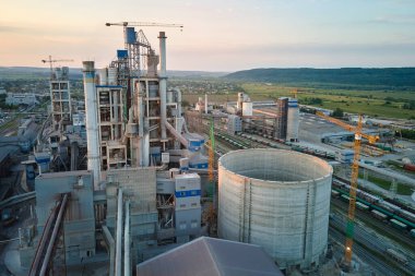 Yüksek fabrika yapısı olan çimento fabrikası ve endüstriyel üretim bölgesinde kule vinçleri var. Üretim, küresel sanayi ve hava kirliliği kavramı.