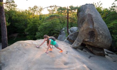 Hiker woman clambering on rocky mountain footpath in evening nature. Lonely female traveler traversing hard wilderness trail. Healthy lifestyle and sport concept.