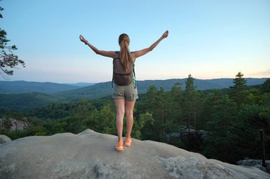 Yürüyüşçü kadın dağ yolunda dinleniyor. Doğa yürüyüşü sırasında el kaldırıyor ve akşam doğasının tadını çıkarıyor. Yüksek tepe yolundan geçen yalnız bir kadın gezgin. Sağlıklı yaşam tarzı kavramı.