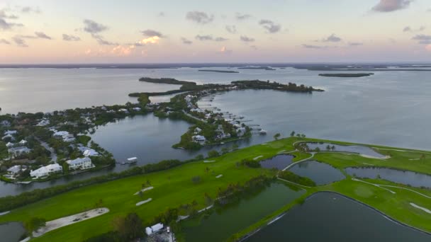 夕方にフロリダ州南西部のガスパリラ島の小さな町ボカ グランデの緑の芝生と大きなゴルフコースフィールドの空中ビュー — ストック動画