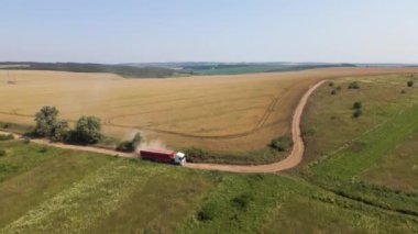 Tarım buğday tarlaları arasında toprak yolda giden kargo kamyonunun hava görüntüsü çok toz yapıyor. Hasat mevsiminde hasatçıların topladığı tahıl naklinden sonra..
