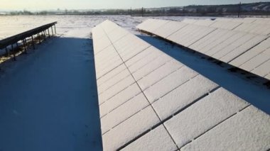Aerial view of sustainable electrical power plant with solar photovoltaic panels covered with snow in winter for producing clean energy. Concept of low effectivity of renewable electricity in north.