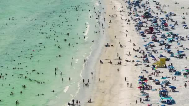 アメリカのサラソータで観光客でいっぱいの白い砂浜とシエスタキービーチの上からの眺め 多くの人々はメキシコ湾の水で泳いだり 暖かいフロリダの太陽の下でリラックスして休暇を楽しんでいます — ストック動画
