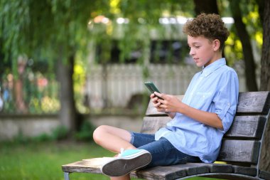 Yaz parkında akıllı telefonuyla oyun oynayan genç bir çocuk. Elektronik cihazlar konseptinden bağımlılık.