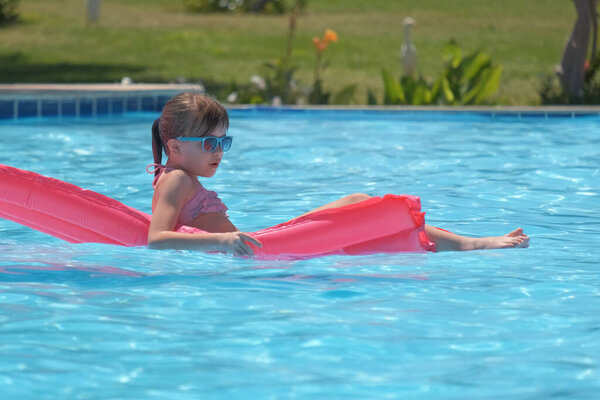 Young child girl relaxing on summer sun swimming on inflatable air mattress in swimming pool during tropical vacations. Summertime activities concept.