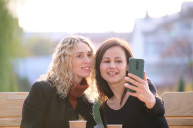 Neşeli kız arkadaşlar şehirdeki kafede cep telefonlarıyla selfie çekiyorlar. Bayan arkadaşlar sıcak bir günde birlikte dışarıda vakit geçiriyorlar..