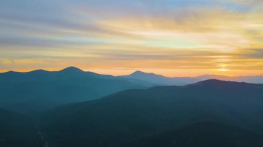 Gün batımında gün batımında parlak güneş ışınlarıyla karanlık dağ tepelerinin havadan görünüşü. Akşamları sisli tepeler ve sisli vadiler.