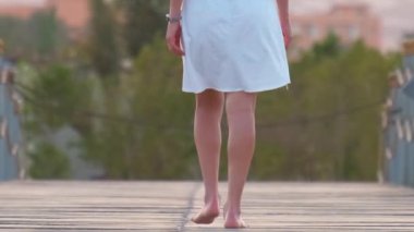 Akşamları uzun iskelede yürüyen beyaz elbiseli genç bir kadın. Tatiller ve seyahat konsepti.