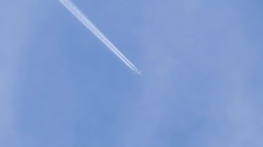 Uzaktaki yolcu uçağı mavi gökyüzünde yüksek irtifada uçarken beyaz bulutlar ardında iz bırakıyor. Hava yolculuğu konsepti.