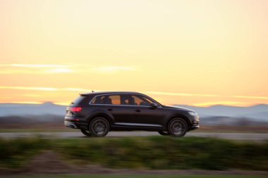 Gün batımında şehirlerarası yolda hızla giden bir SUV arabası. Akşamları otoyol trafiği.