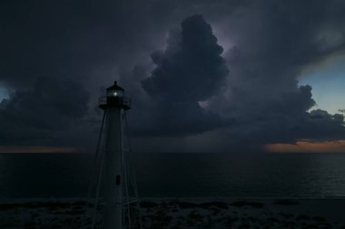 Deniz kıyısındaki uzun deniz feneri fırtınalı bir gecede ticari gemilerin seyrüsefer için yanıp sönen ışık. Okyanus üzerinde şimşekler çakan fırtına gemiler için tehlike arz ediyor..