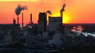 Üretim sürecinden kaynaklanan dumanlı büyük fabrika yapısı üretim sahasında çevre kirliliği yaratan atmosferi yükseltiyor. Gün batımında sanayi bölgesi.