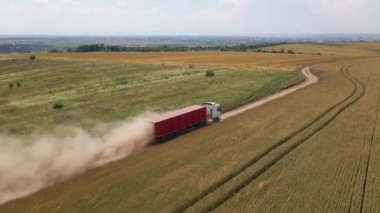 Tarım buğday tarlaları arasında toprak yolda giden kargo kamyonunun hava görüntüsü çok toz yapıyor. Hasat mevsiminde hasatçıların topladığı tahıl naklinden sonra..