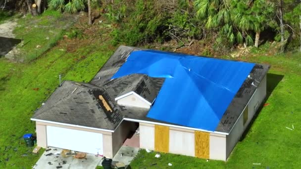 ハリケーンイアンの家の屋根の損傷の空中ビューは アスファルトの帯状疱疹の交換まで雨の水漏れに対する青の保護タープで覆われて — ストック動画