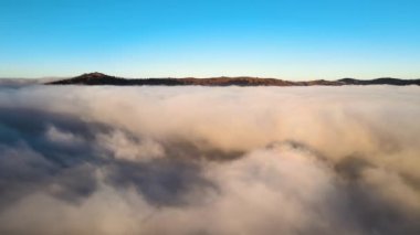 Güneşin doğuşuyla dumanlı dağ tepelerini kaplayan sisli ve hızlı bulutların üzerindeki hava manzarası.