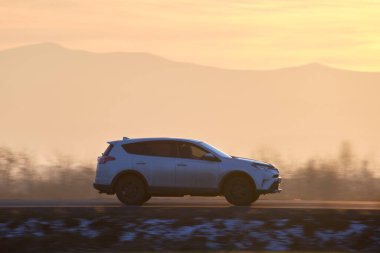 Gün batımında şehirlerarası yolda hızla giden bir SUV arabası. Akşamları otoyol trafiği.