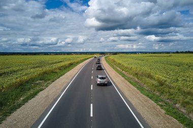 Hızlı giden arabalarla yeşil tarımsal alanlar arasındaki şehirlerarası yolun havadan görünüşü. Karayolu trafiğinin insansız hava aracı görüntüsü.