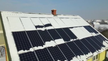 Aerial view of house roof with solar panels covered with snow melting down in winter end for producing clean energy. Concept of low effectivity of renewable electricity in northern region.