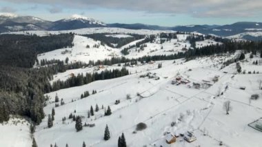 Soğuk dağlarda karla kaplı ormanlar arasında küçük köy evleri olan kış manzarası.