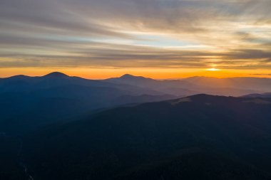 Gün batımında gün batımında parlak güneş ışınlarıyla karanlık dağ tepelerinin havadan görünüşü. Akşamları sisli tepeler ve sisli vadiler.