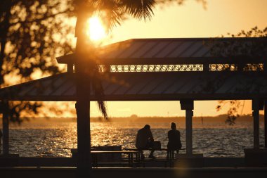 Gün batımında halk parkında, deniz kıyısındaki oyuk çatı altında dinlenen insanların karanlık silueti..