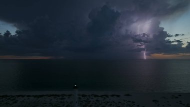 Deniz kıyısındaki uzun deniz feneri fırtınalı bir gecede ticari gemilerin seyrüsefer için yanıp sönen ışık. Okyanus üzerinde şimşekler çakan fırtına gemiler için tehlike arz ediyor..
