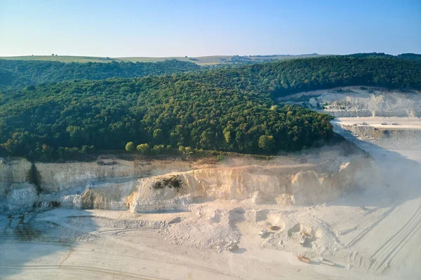 Aerial view of open pit mining site of limestone materials extraction for construction industry with excavators and dump trucks.