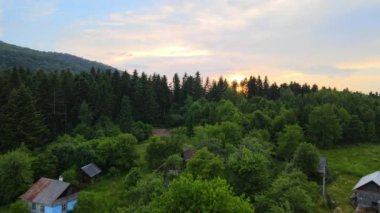 Sonbahar gündoğumunda ormanlık çam ağaçlarıyla kaplı sisli, karanlık dağ tepeleri arasındaki küçük köy evlerinin hava manzarası. Şafak vakti ışıldayan ışıklarıyla güzel vahşi ormanlık.