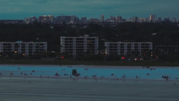 フロリダ州 米国のサラソータ市でのシエスタキービーチの高い角度の視点夜 高層ビルやオフィスビルが立ち並ぶ遠く離れたダウンタウンやホテルが並ぶ緑豊かな郊外 — ストック動画