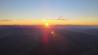 Gün batımında gün batımında parlak güneş ışınlarıyla karanlık dağ tepelerinin havadan görünüşü. Akşamları sisli tepeler ve sisli vadiler.