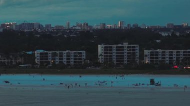 Aerial view of Siesta Key beach with white sands and distant downtown of Sarasota city in Florida, USA at night. High skyscrapers and office buildings on horizon.