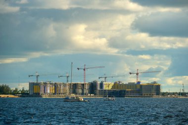 Deniz körfezi kıyısındaki inşaat alanındaki yüksek konut binalarının vinçleri ve iskelet yapısı. Rıhtımda gayrimenkul geliştirme.