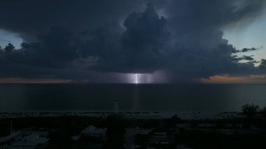 Deniz kıyısındaki uzun deniz feneri fırtınalı bir gecede ticari gemilerin seyrüsefer için yanıp sönen ışık. Okyanus üzerinde şimşekler çakan fırtına gemiler için tehlike arz ediyor..