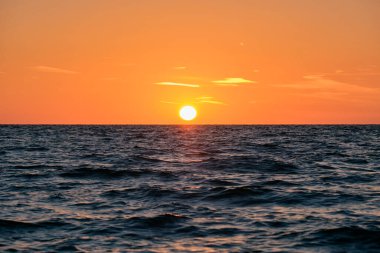 Okyanus batımı. Büyük beyaz güneş dramatik parlak gökyüzü arka planında, yumuşak akşam bulutu denizin üstünde kara su.