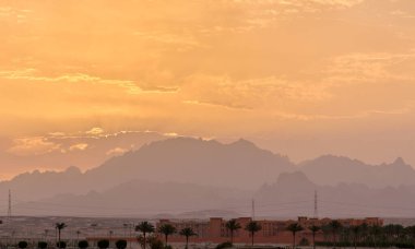 Uzak otel kompleksiyle gün batımı manzarası Mısır çölündeki karanlık dağ zirvelerine karşı.
