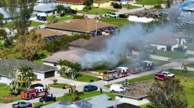 View from above of burning private house on fire and firefighters extinguishing flames after short circuit caused to ignite roof damaged by hurricane Ian wind. Home disaster in Florida suburban area.