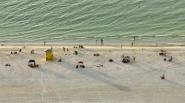 High angle view of crowded Siesta Key beach in Sarasota, USA. Many people enjoing vacations time swimming in ocean water and relaxing on warm Florida sun at sundown.