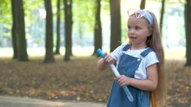 Yeşil Park 'ın dışında sabun köpüğü üfleyen küçük mutlu kız çocuğu. Açık hava yaz aktiviteleri konsepti.