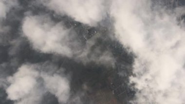 Fırtınadan önce, şişkin kümülüs bulutlarıyla kaplı uzak şehrin yüksek irtifasından gelen hava manzarası. Bulutlu havada uçak manzarası.