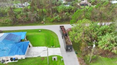 Top view of Hurricane Ian aftermath recovery dump truck picking up tree branches debris from Florida rural streets. Dealing with consequences of natural disaster.