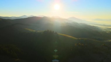 View from above of ukrainian Carpathian mountains with wooded hills and traditional village homes at autumnal sunset. Brightly illuminated pine woods with scattered local settlement houses.