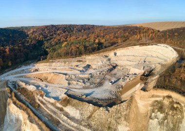 Kazı makineleri ve çöp kamyonlarıyla inşaat endüstrisi için kumtaşı malzemelerinden oluşan açık maden manzarası. Madencilik ve kullanışlı mineral üretiminde ağır ekipman.