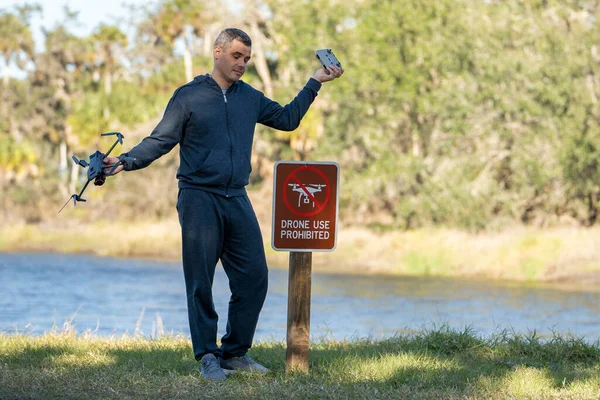 stock image Man is sad that he is not allowed to fly his quadcopter state park no drone area. Operator is unauthorised to use UAS near restriction sign.