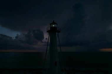 Deniz kıyısındaki uzun deniz feneri fırtınalı bir gecede ticari gemilerin seyrüsefer için yanıp sönen ışık. Okyanus üzerinde şimşekler çakan fırtına gemiler için tehlike arz ediyor..