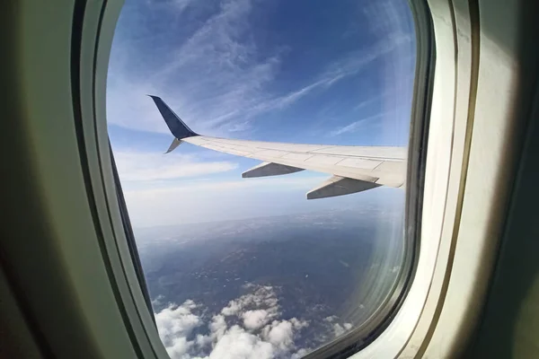 View through airplane window of commercial jet plane wing flying high in the sky. Air travelling concept.