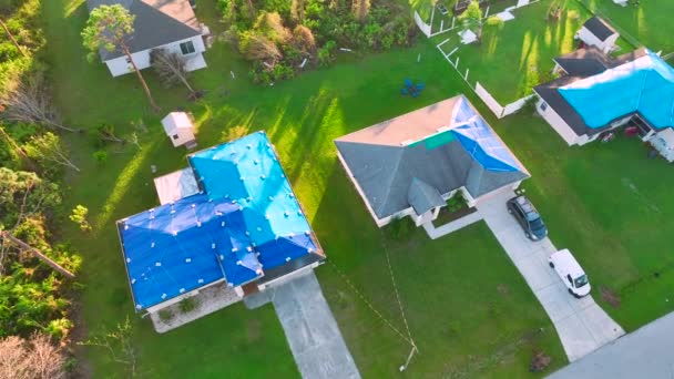ハリケーンイアンの家の屋根に損傷の空中ビューアスファルトの帯状疱疹の交換まで雨の水漏れに対する青の保護タープで覆われて — ストック動画