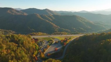 Top view of large rest area between golden fall forest near busy multilane american freeway with fast moving cars and trucks. Recreational resting place during interstate traveling thru USA mountains.