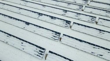 Aerial view of sustainable electrical power plant with solar photovoltaic panels covered with snow in winter for producing clean energy. Concept of low effectivity of renewable electricity in north.