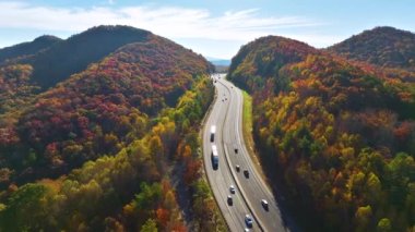 I-40 freeway road leading to Asheville in North Carolina over Appalachian mountain pass with yellow fall forest and fast moving trucks and cars. Concept of high speed interstate transportation.